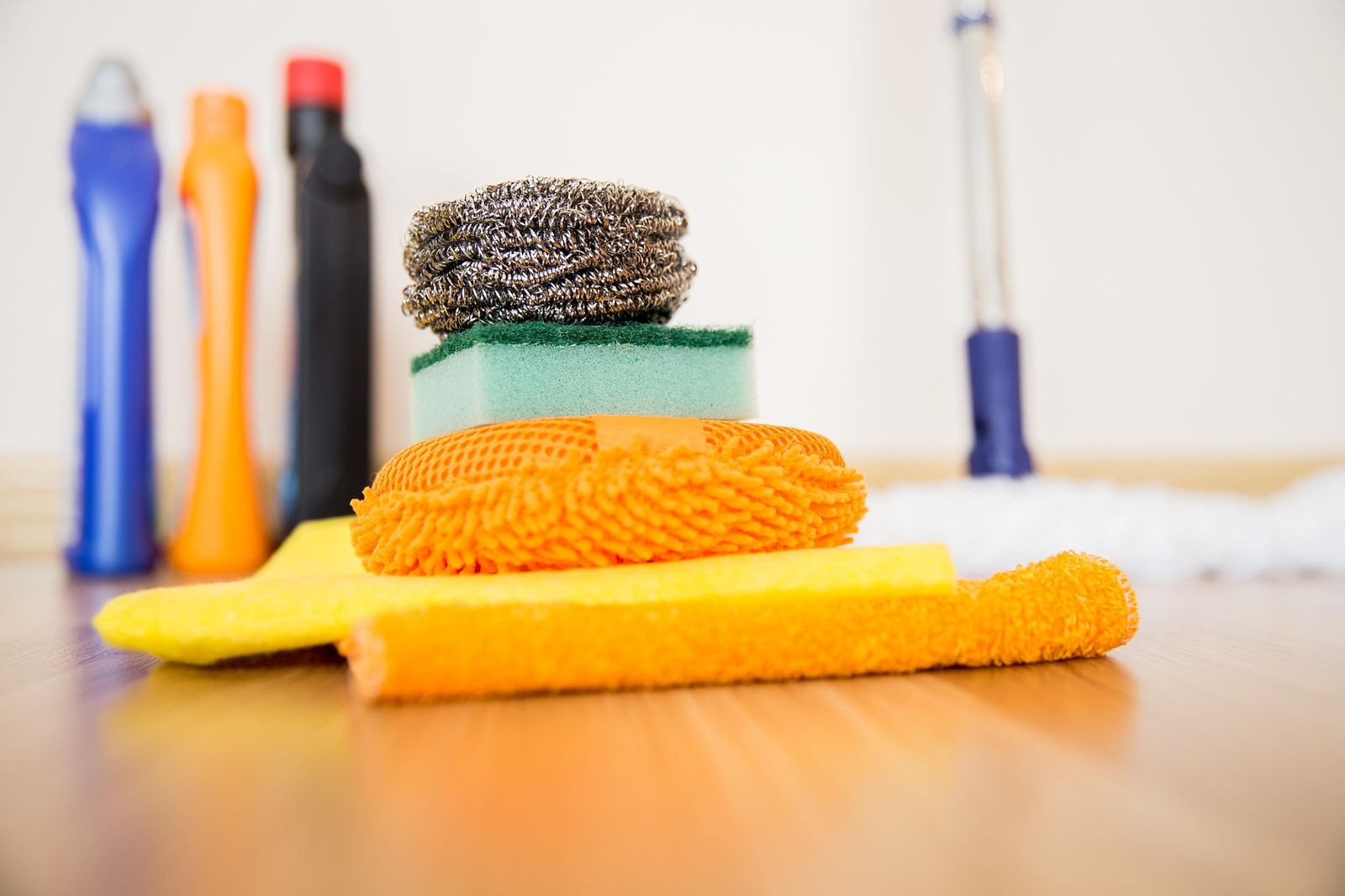 Cleaning bottles, sponges, a scrubber and microfiber cloths on a wood floor