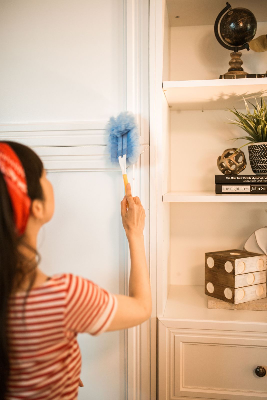 Woman dusting white wall trim with a duster